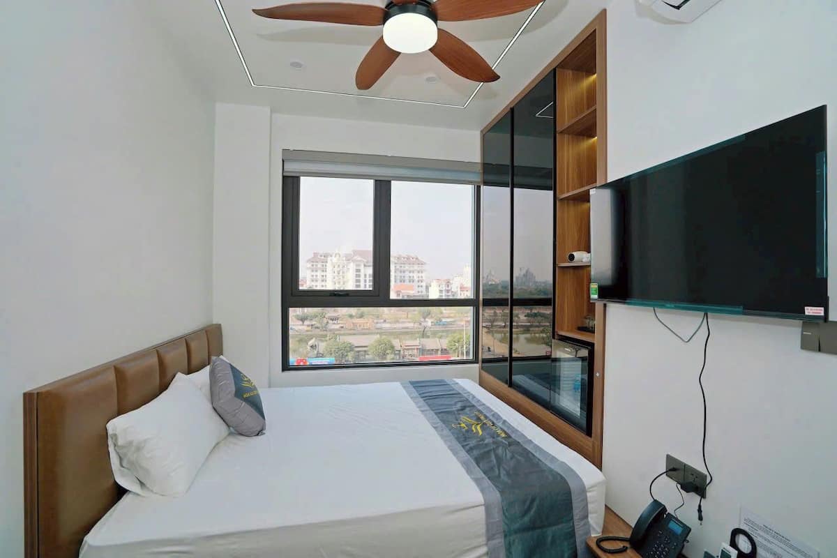 Een moderne hotelkamer met een bed, een plafondventilator, een groot raam, een televisie en een telefoon.