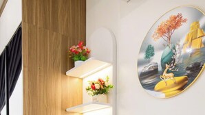 Un comptoir de réception d’hôtel avec un téléphone, une petite poubelle et une étagère fixée au mur, ornée de fleurs.