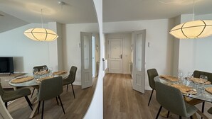 Ein Essbereich mit einem runden Tisch, Stühlen und einem Fernseher. Zwei Türen führen in andere Räume.