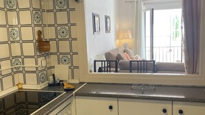 Una cocina con estufa, armarios y ventana con vista a un balcón con sofá.