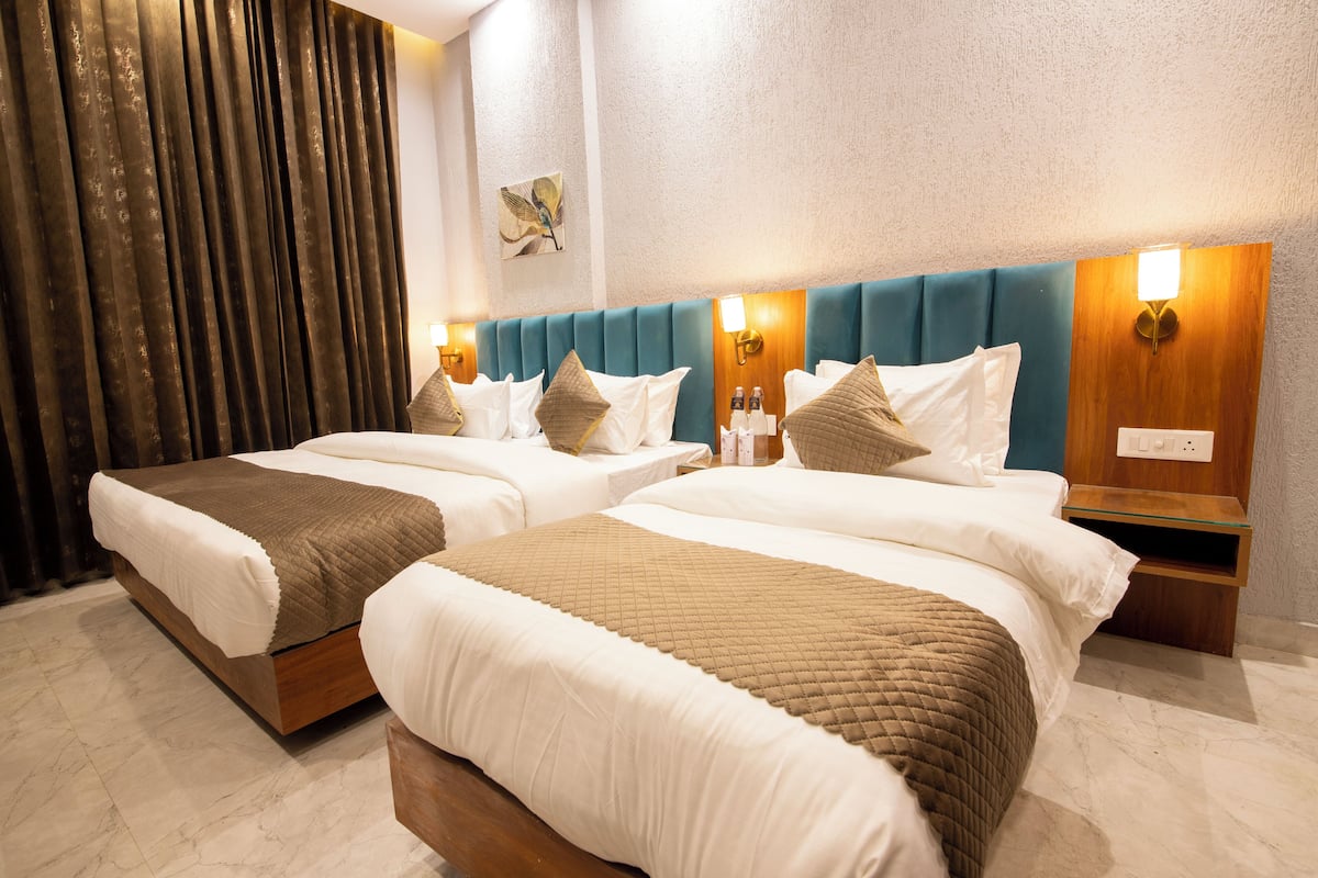 Ein Hotelzimmer mit zwei Betten, jeweils mit Holz Kopfteilen, weißer Bettwäsche und einer braunen gesteppten Tagesdecke. Es gibt Nachttische mit Lampen und eine Wandleuchte.