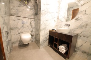 Un baño con pared de mármol, inodoro, lavamanos y espejo.
