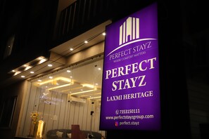 Un letrero de hotel con el nombre 'Perfect Stayz' y 'Laxmi Heritage'.