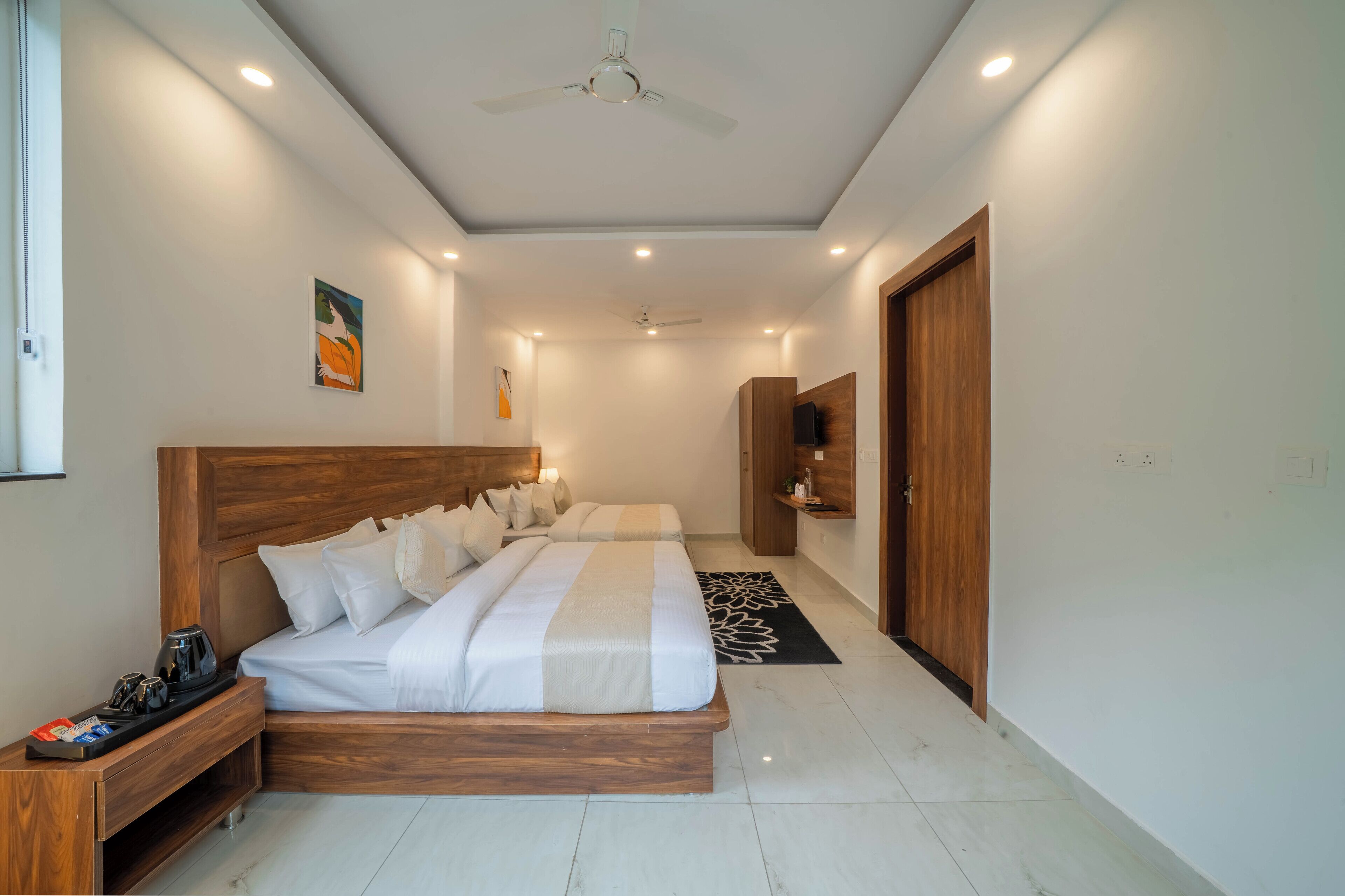 Une chambre d’hôtel moderne avec un grand lit, des tables de chevet, un ventilateur de plafond et un téléviseur posé sur une étagère en bois.