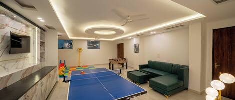 Ein modernes Wohnzimmer mit Tischtennisplatte, grünem Sofa und Kicker.