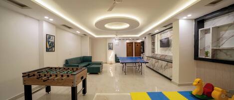 A modern living room with a foosball table, a ping pong table, and a play area with colorful foam mats.