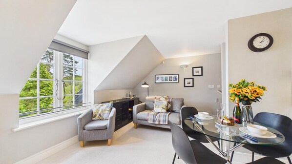 Une chambre à coucher de style loft moderne, avec un plafond en pente, un coin repas doté d’une table en verre et une vue sur la verdure grâce à une grande fenêtre.