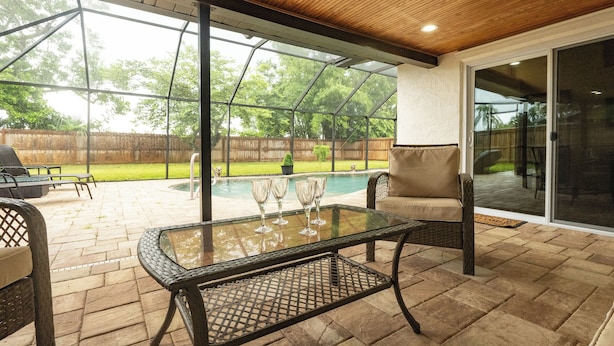 Ein überdachter Patio-Bereich mit einem Glastisch, Stühlen und einem Pool im Hintergrund.