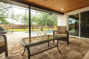 Een overdekt terras met een glazen tafel, stoelen en een zwembad op de achtergrond.