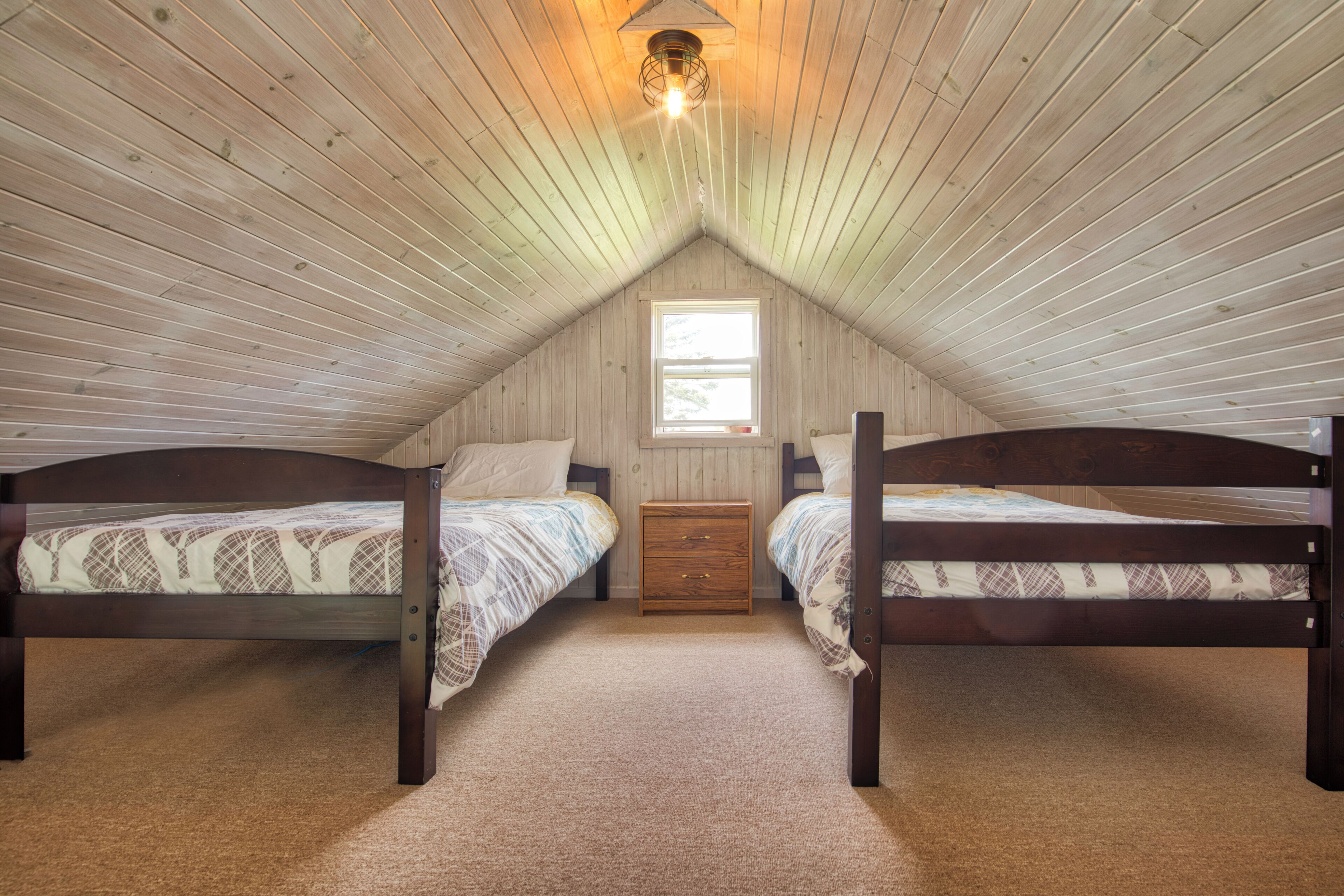 A bedroom with two beds, a window, and a wooden ceiling.