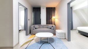Een moderne hotelkamer met een grijze bank, een witte salontafel, een klein wit poef en een bed.