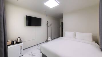 A hotel room with a bed, a TV mounted on the wall, a coffee machine, and a small table with a kettle and a tissue box.