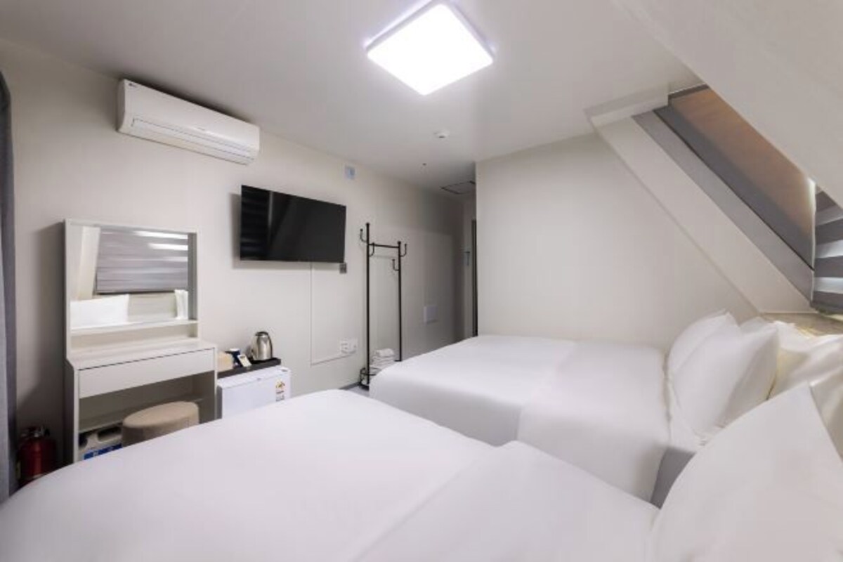 A hotel room with two beds, a TV, a mirror, a small desk, and a staircase.
