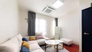 Een moderne hotelkamer met een bank, twee ronde tafels, een klein poufje, een bed en een deur.