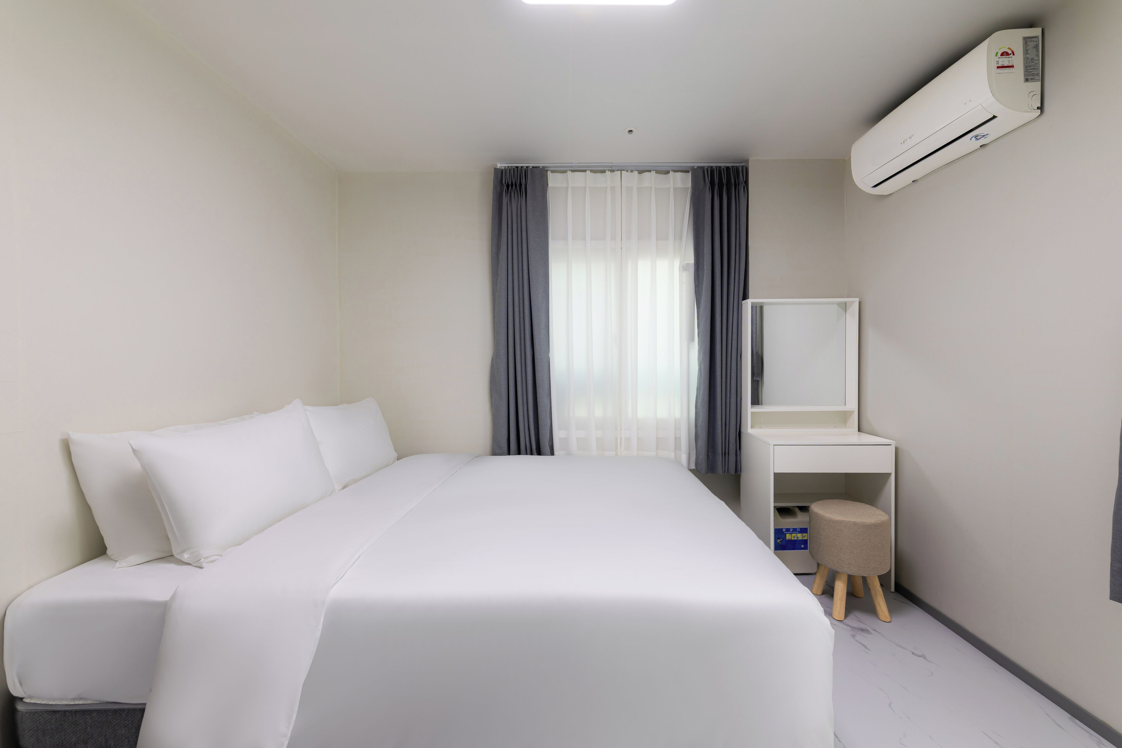 A hotel room with a bed, a desk, a chair, an air conditioning unit, and a window with curtains.
