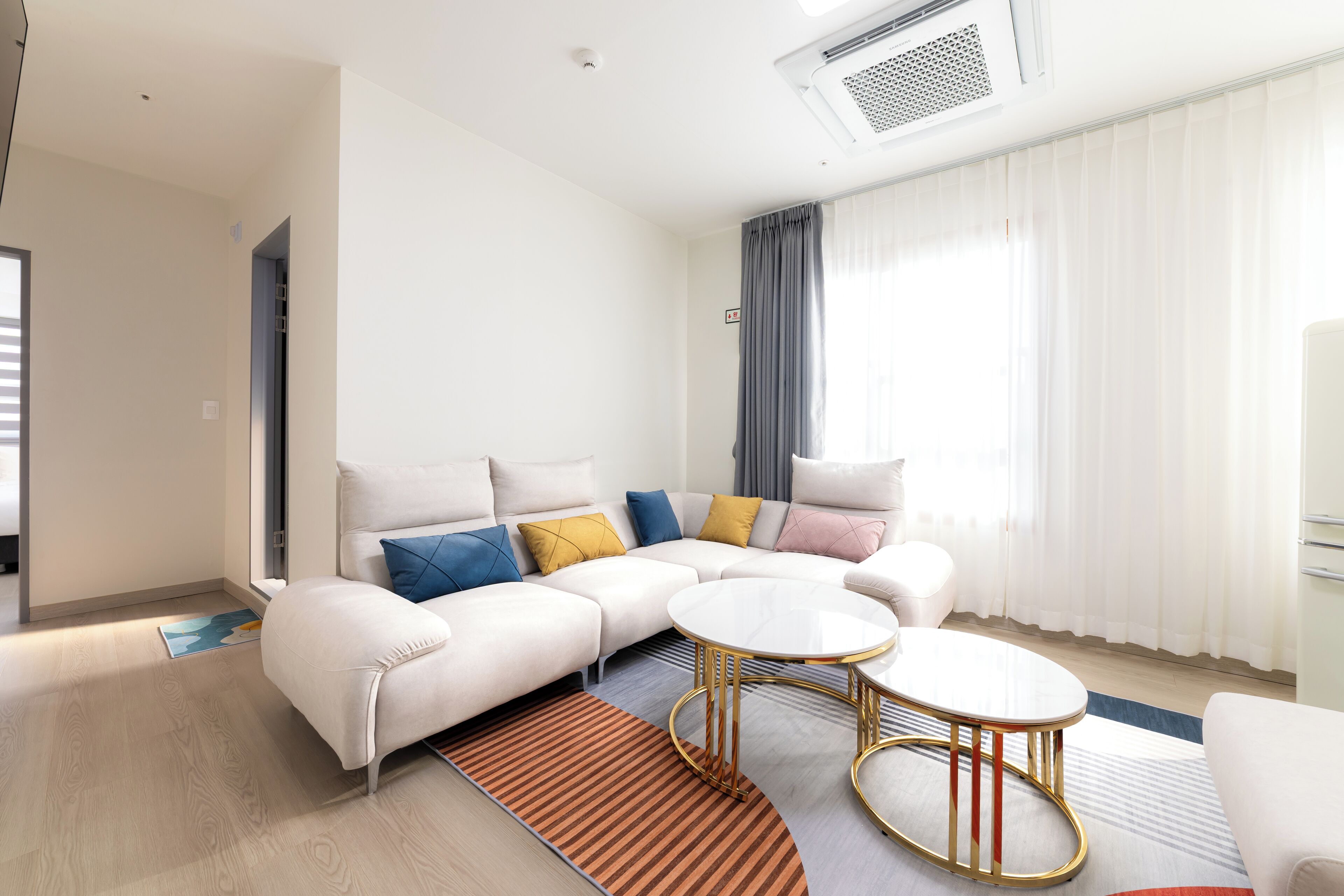 A modern living room with a sectional sofa, two round coffee tables, and a large window with curtains.