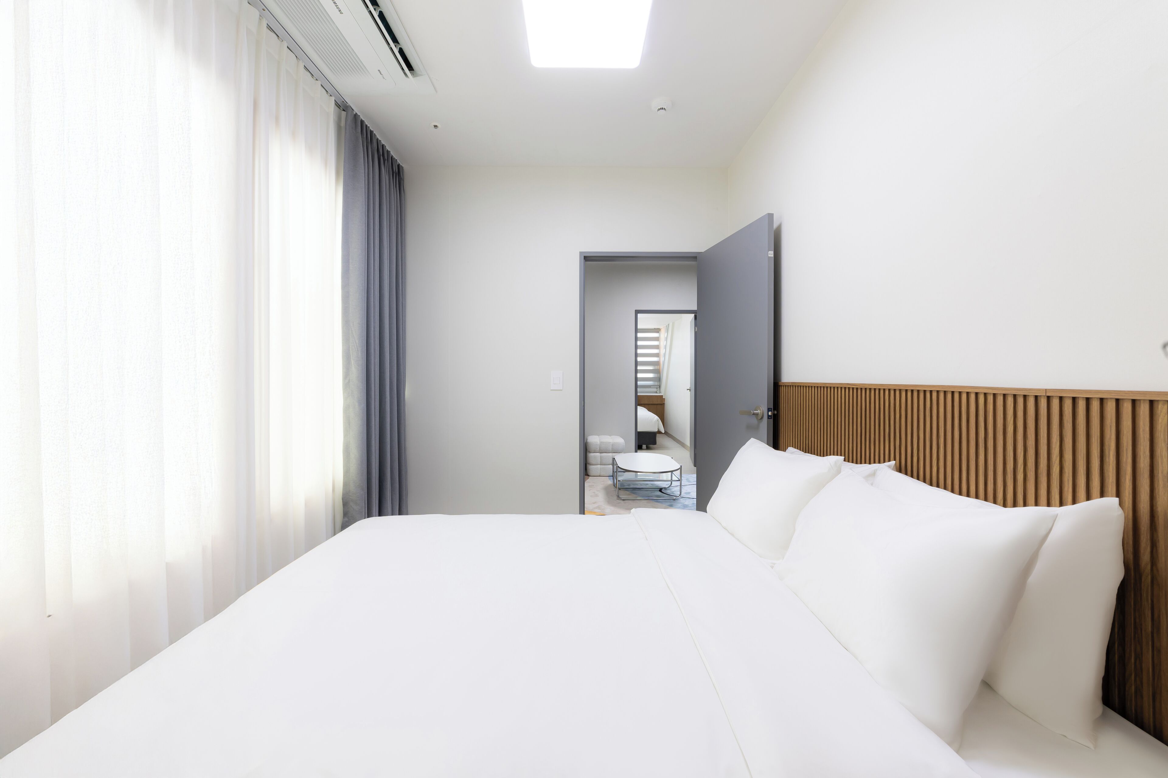 A hotel room with a large bed, a wooden headboard, a bedside table, and a view of a bathroom through an open door.