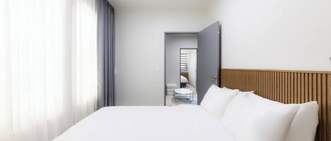 A hotel room with a large bed, a wooden headboard, a bedside table, and a view of a bathroom through an open door.