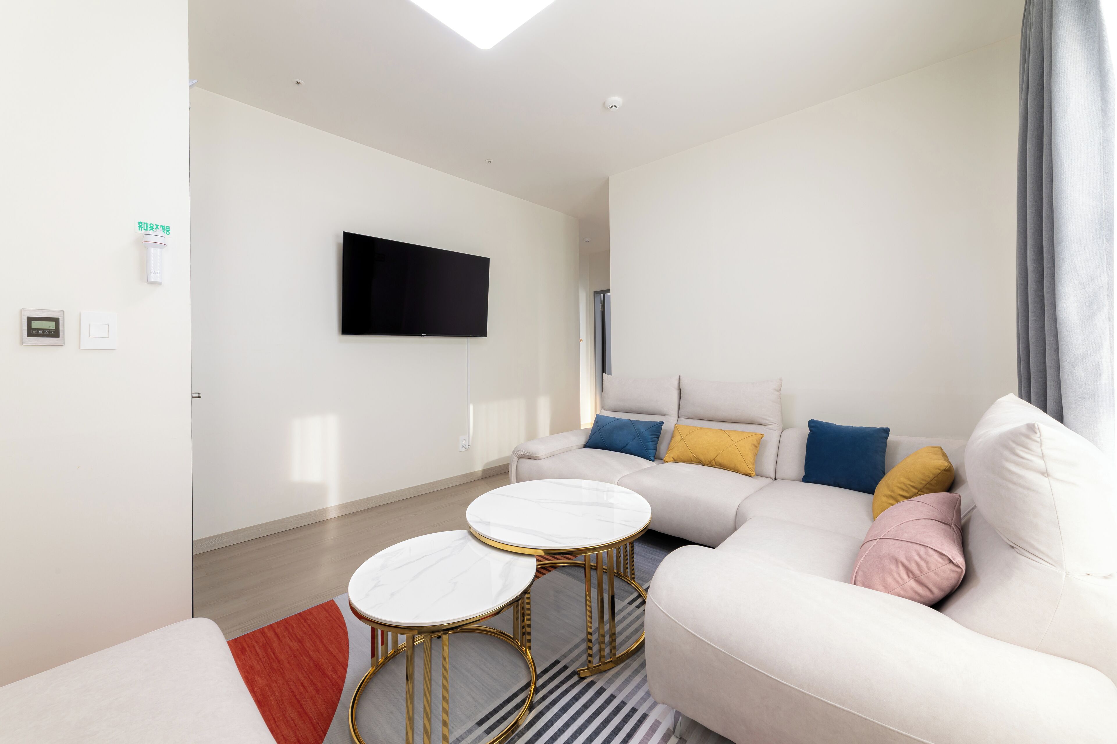 A modern living room with a sofa, two round tables, a flat-screen TV, and a red rug.