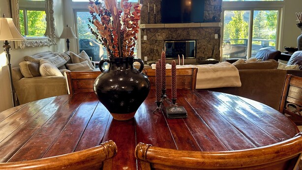 Un coin repas avec une table ronde en bois, un vase noir contenant des fleurs séchées et une cheminée surmontée d’un téléviseur à écran plat.