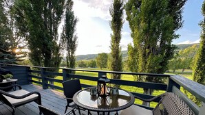 Une terrasse dotée de meubles en osier, d’une table ronde et offrant une vue sur un paysage verdoyant.