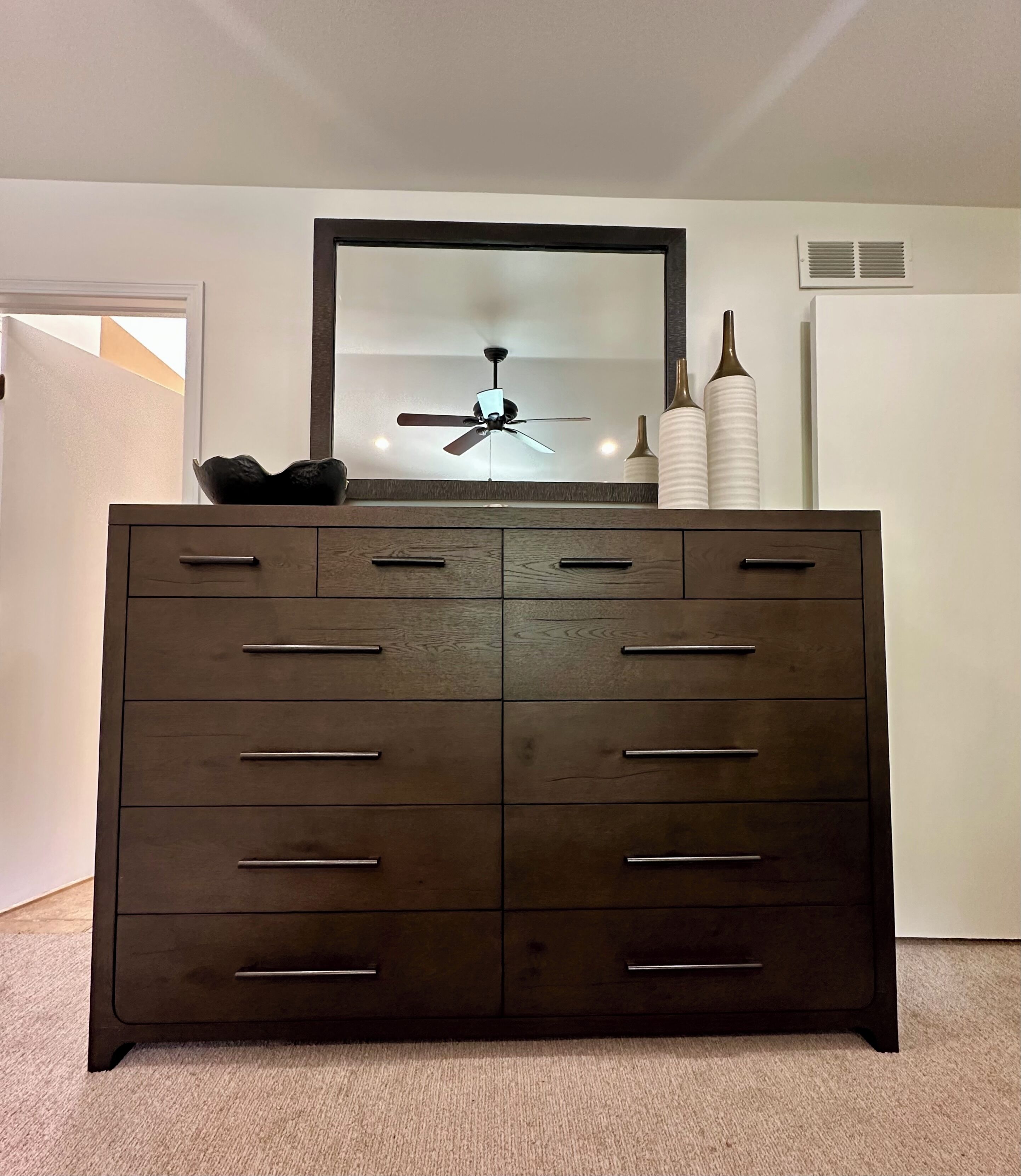 Une commode en bois foncé, dotée de nombreux tiroirs et surmontée d’un miroir.