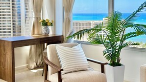 A modern room with a view of the ocean, a wooden chair, a small table with a vase of flowers, and a large potted plant.