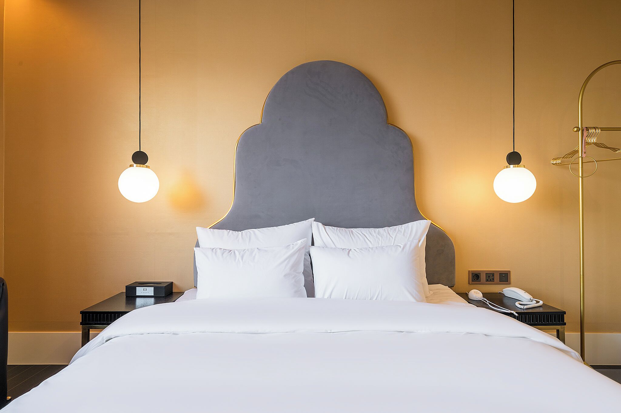 A hotel room with a large bed, two bedside tables, a telephone, and a wall-mounted light fixture.
