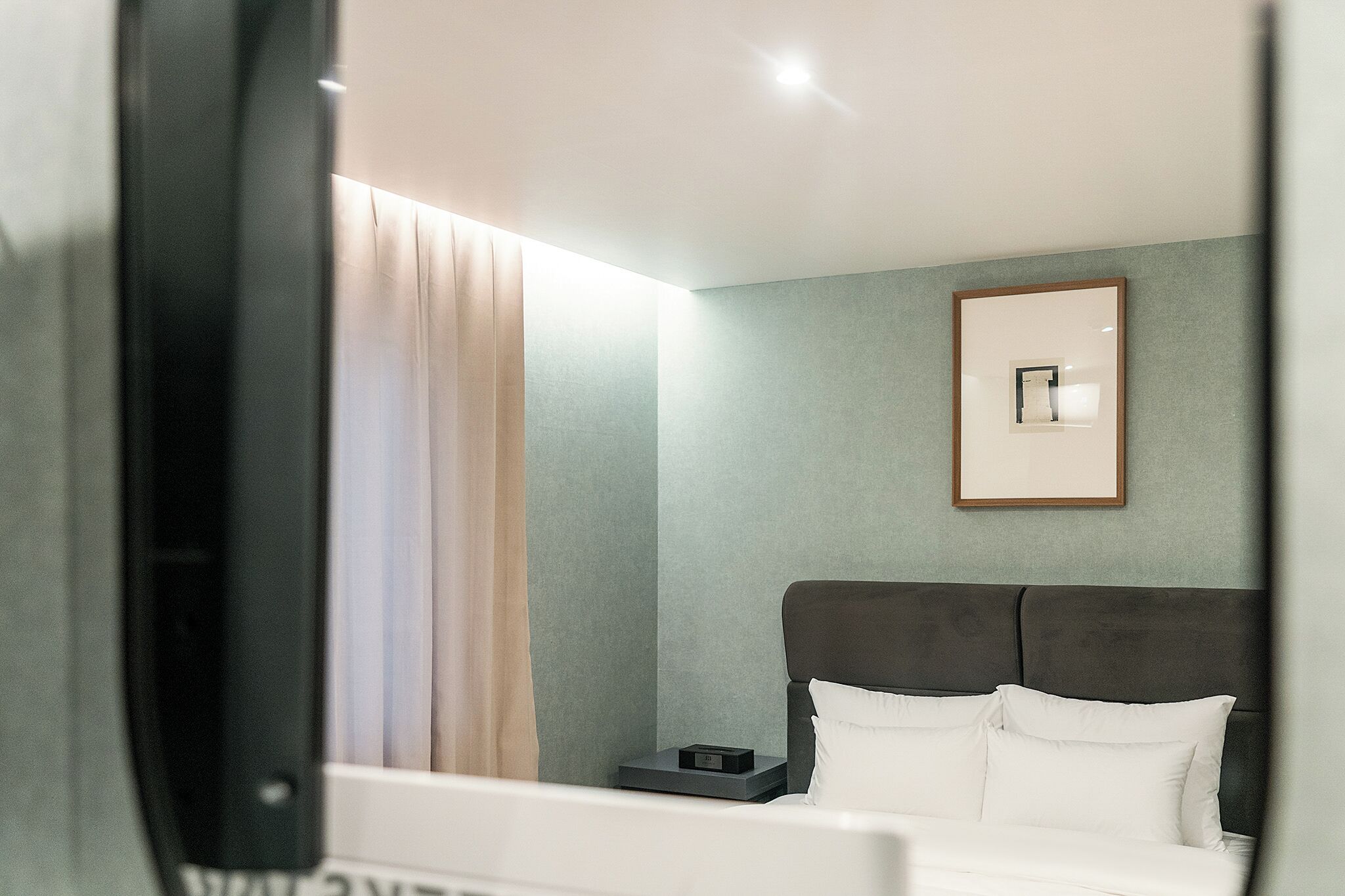 Une chambre d’hôtel avec un lit, une table de chevet, un tableau encadré au mur et une fenêtre avec des rideaux.
