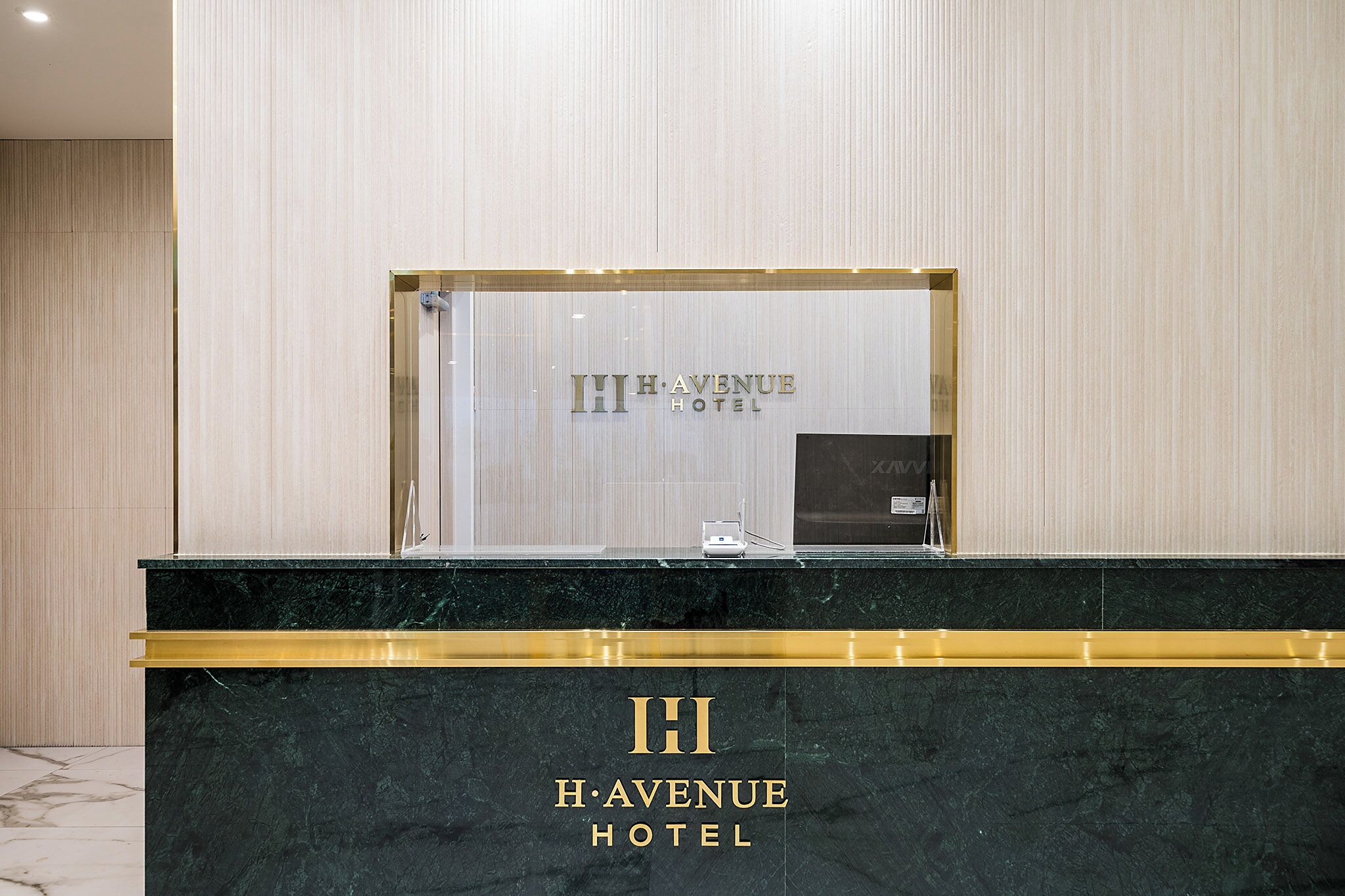 Una recepción con el logotipo de H.AVENU HOTEL, un panel de vidrio y un detalle dorado.
