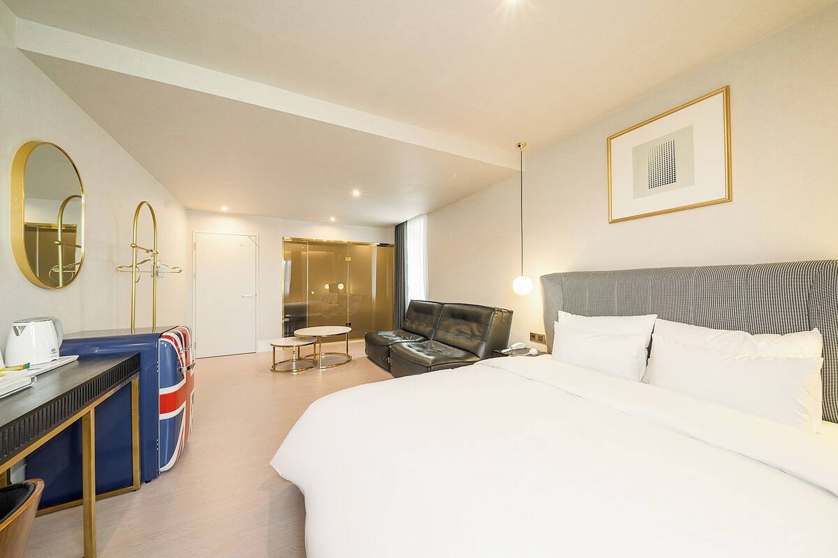 A hotel room with a bed, a desk, a chair, a sofa, a mirror, and a framed picture on the wall.