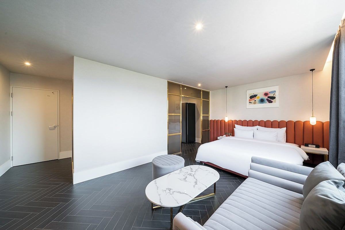 A modern hotel room with a large bed, a seating area with a marble table, and a wardrobe with a mirror.
