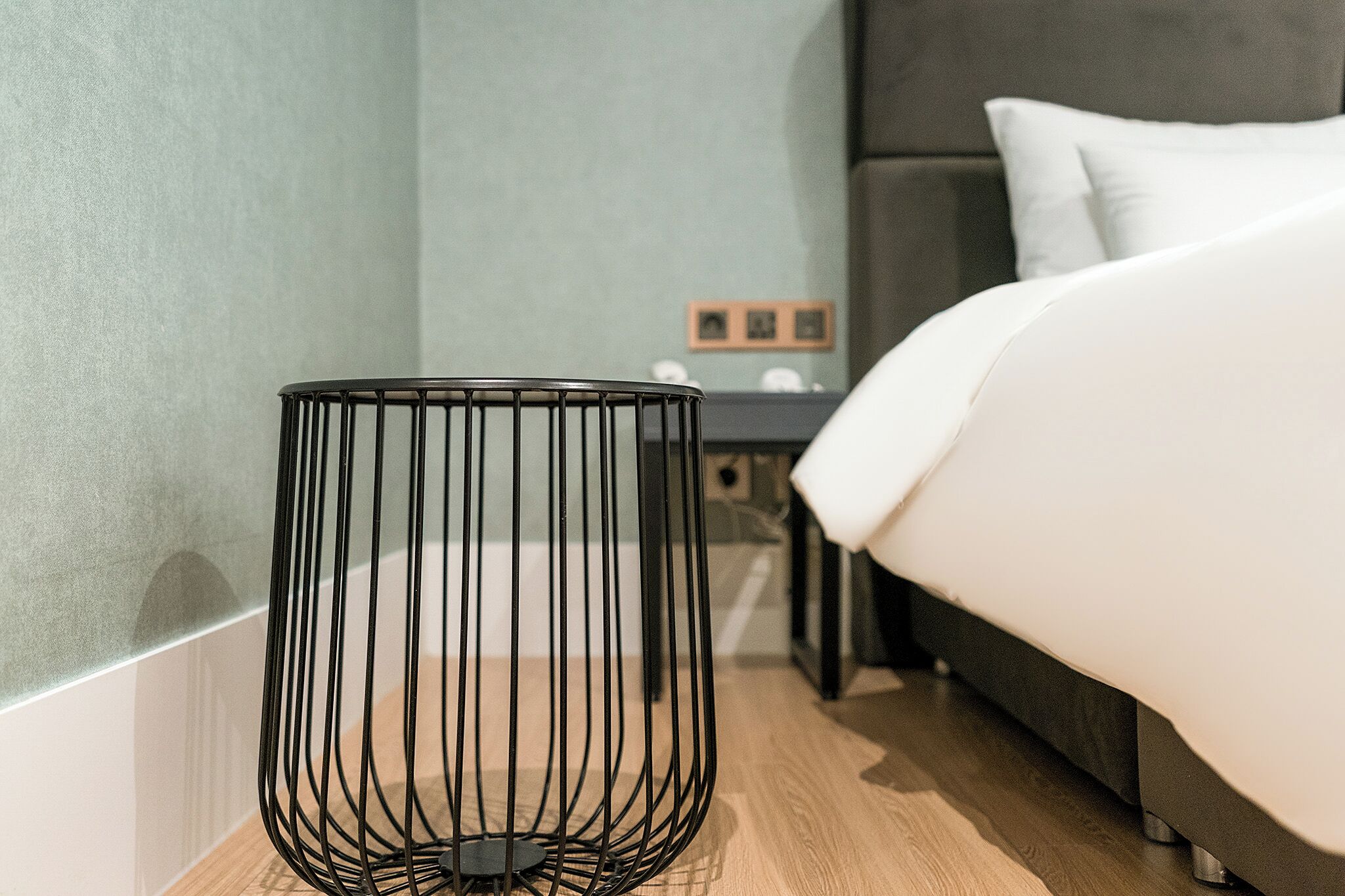 Una habitación de hotel moderna con una cama, una mesita de noche, una cesta de mimbre negra y suelo de madera.