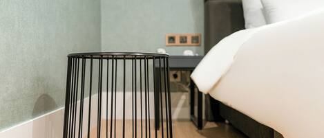 Una habitación de hotel moderna con una cama, una mesita de noche, una cesta de mimbre negra y suelo de madera.