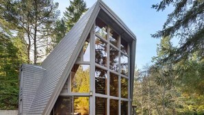 Una casa moderna de madera con forma triangular y grandes ventanales, rodeada de un bosque.