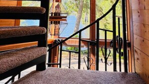 Una escalera de madera con vistas a un lago y árboles a través de amplias ventanas.