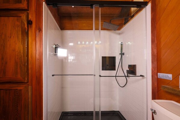 A shower with a glass door, white tiled walls, and wooden paneling.