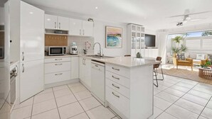 Eine moderne Küche mit weißen Schränken, einer Mikrowelle und einem Spülbecken. Es gibt einen Essbereich mit Tisch und Stühlen, sowie ein großes Fenster mit Blick ins Freie.