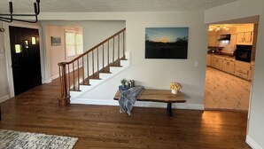 A spacious living area with hardwood floors, a wooden staircase, a dining table with a vase of flowers, and a kitchen visible through an open doorway. - Big Country Escape - 4 Bedroom, Pet Friendly Retreat in Bluewell,  Near Trails (Bluefield)