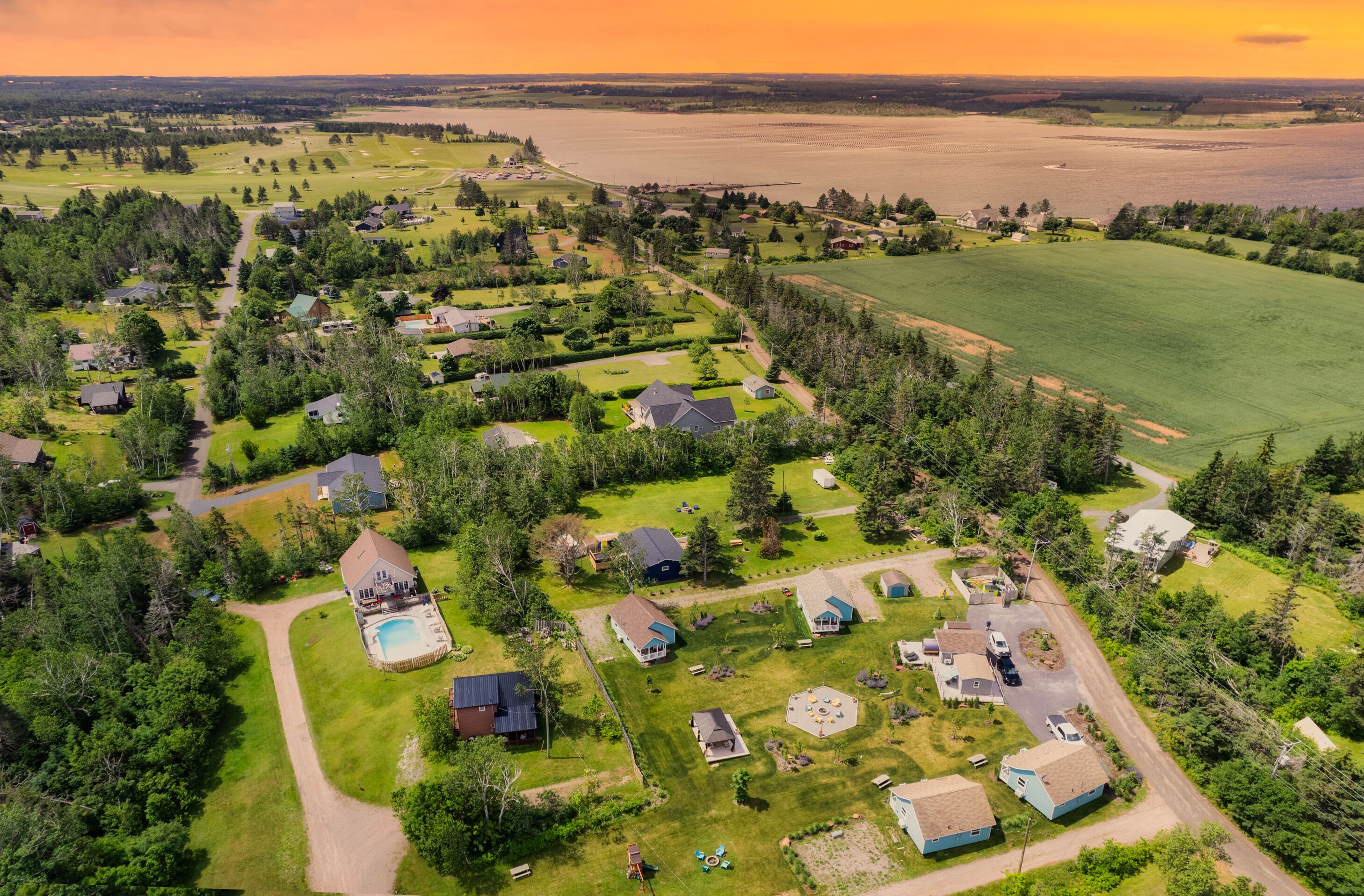 Une vue aérienne d’un quartier résidentiel avec des maisons, une piscine et une grande étendue d’eau en arrière-plan.