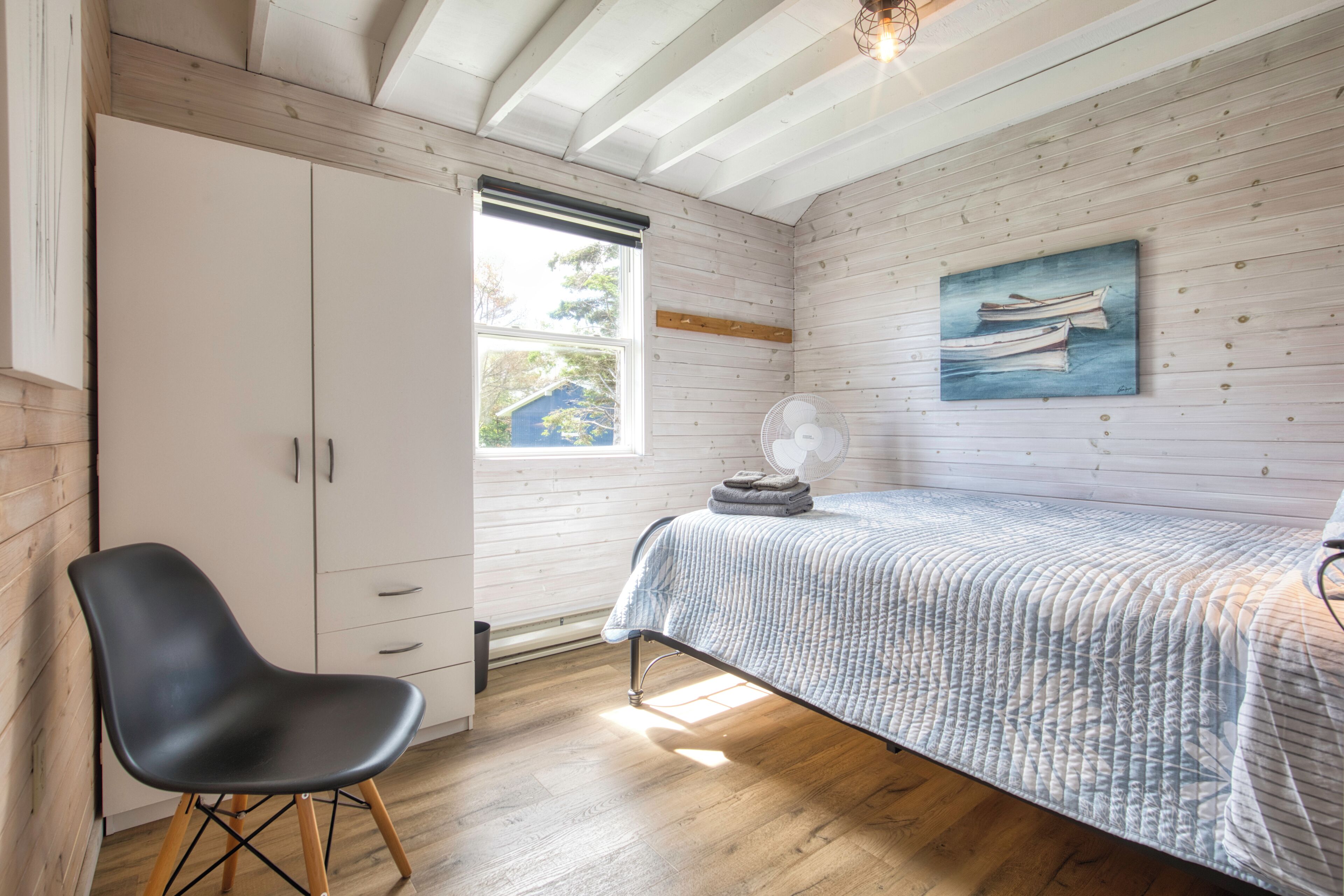 A bedroom with a bed, a chair, a wardrobe, a window, and a painting on the wall.
