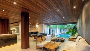 Un área de piscina interior moderna con techo de madera, mesa de billar y asientos.