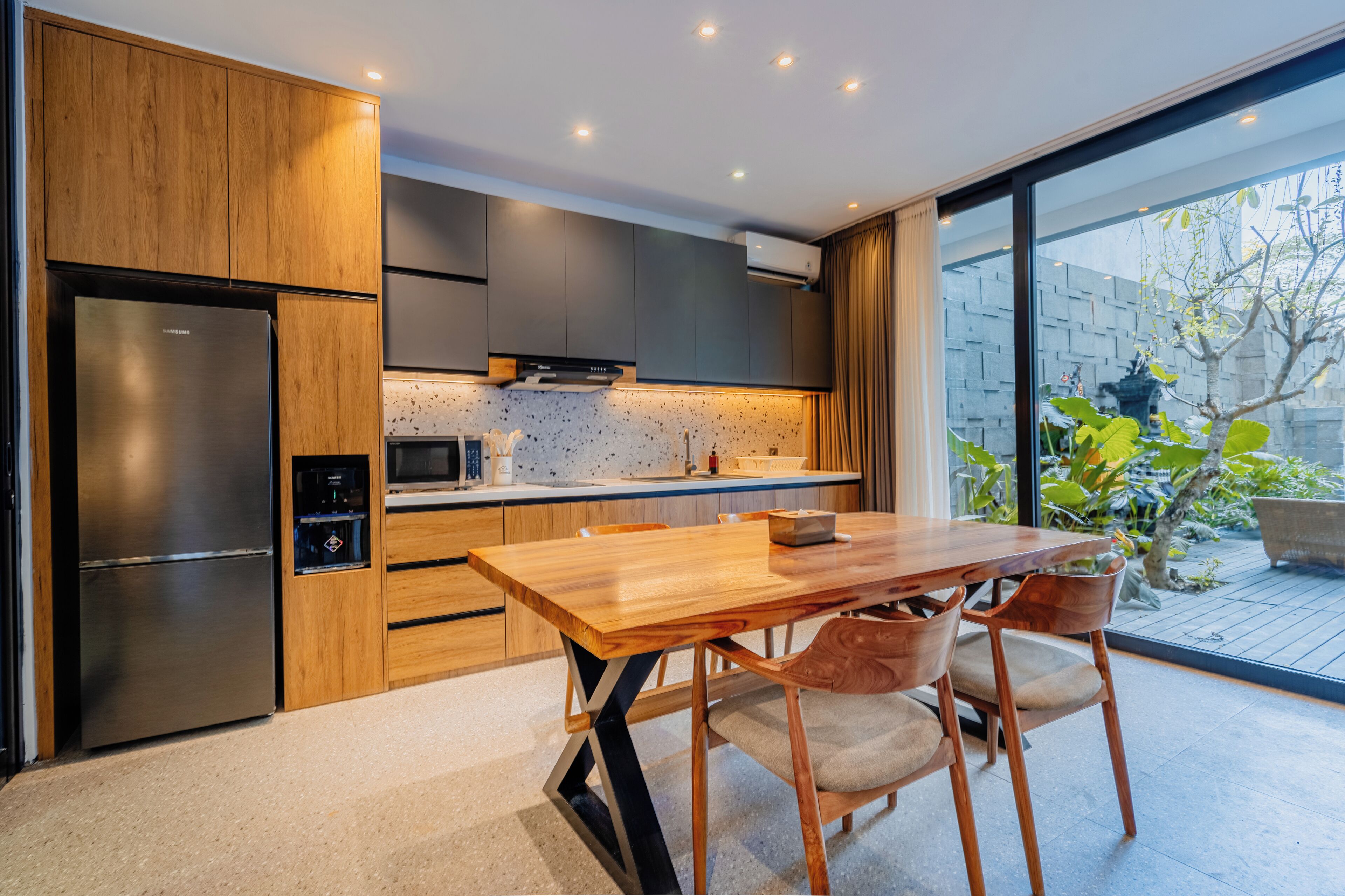 A modern kitchen with wooden cabinets, a stainless steel refrigerator, and a dining area with a wooden table and chairs.