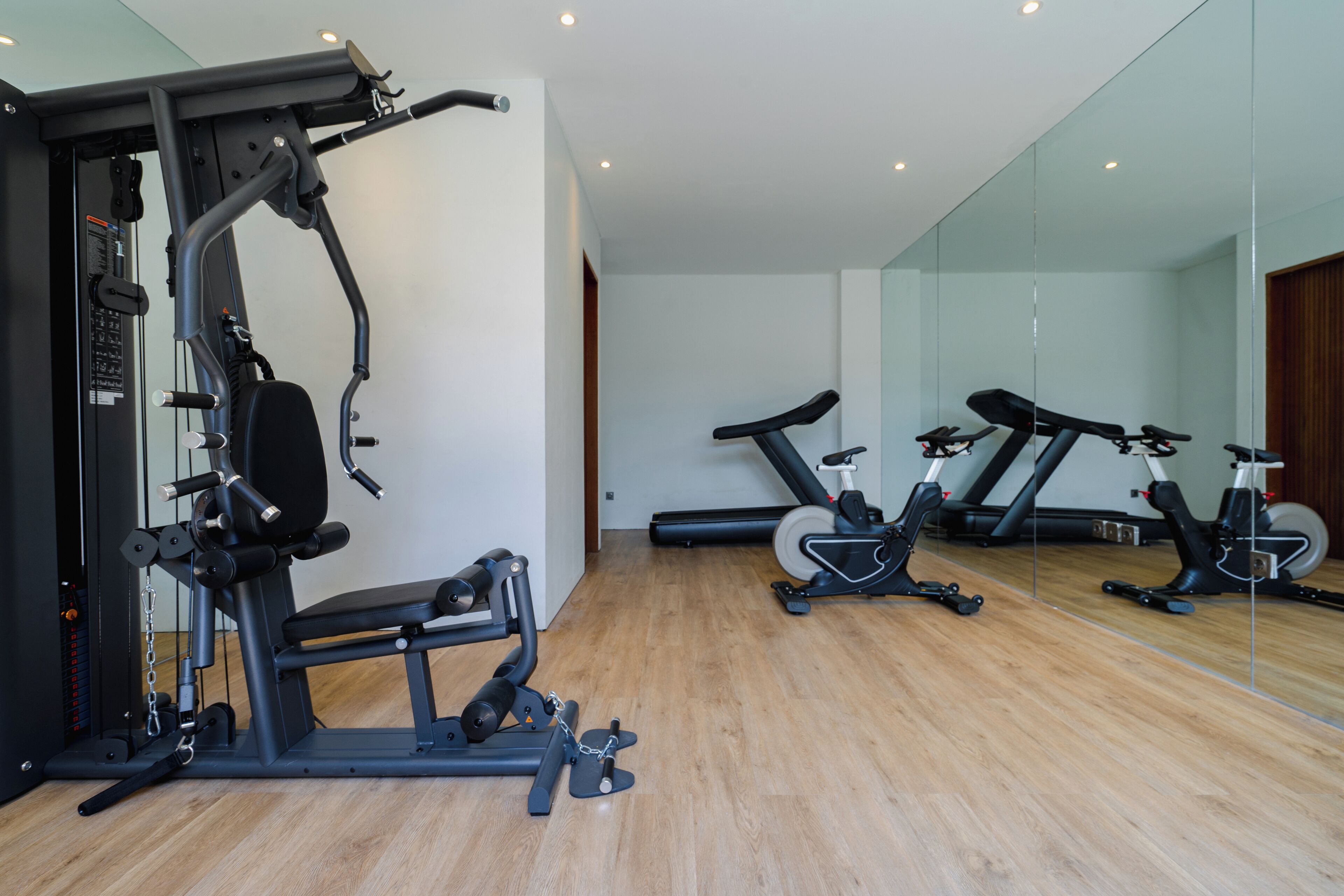 A gym with exercise equipment, a mirror, and wooden flooring.