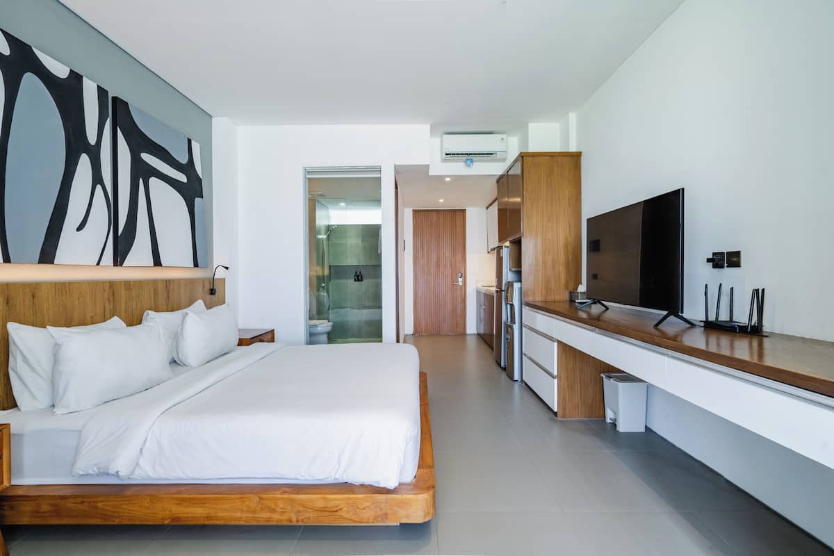 Una habitación de hotel moderna con una cama grande, un cabecero de madera, un televisor de pantalla plana, una cocina con encimera de madera y un cuadro abstracto de gran tamaño en la pared.