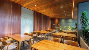 Interior moderno de restaurante con mesas y sillas de madera, pared de piedra y un gran ventanal.