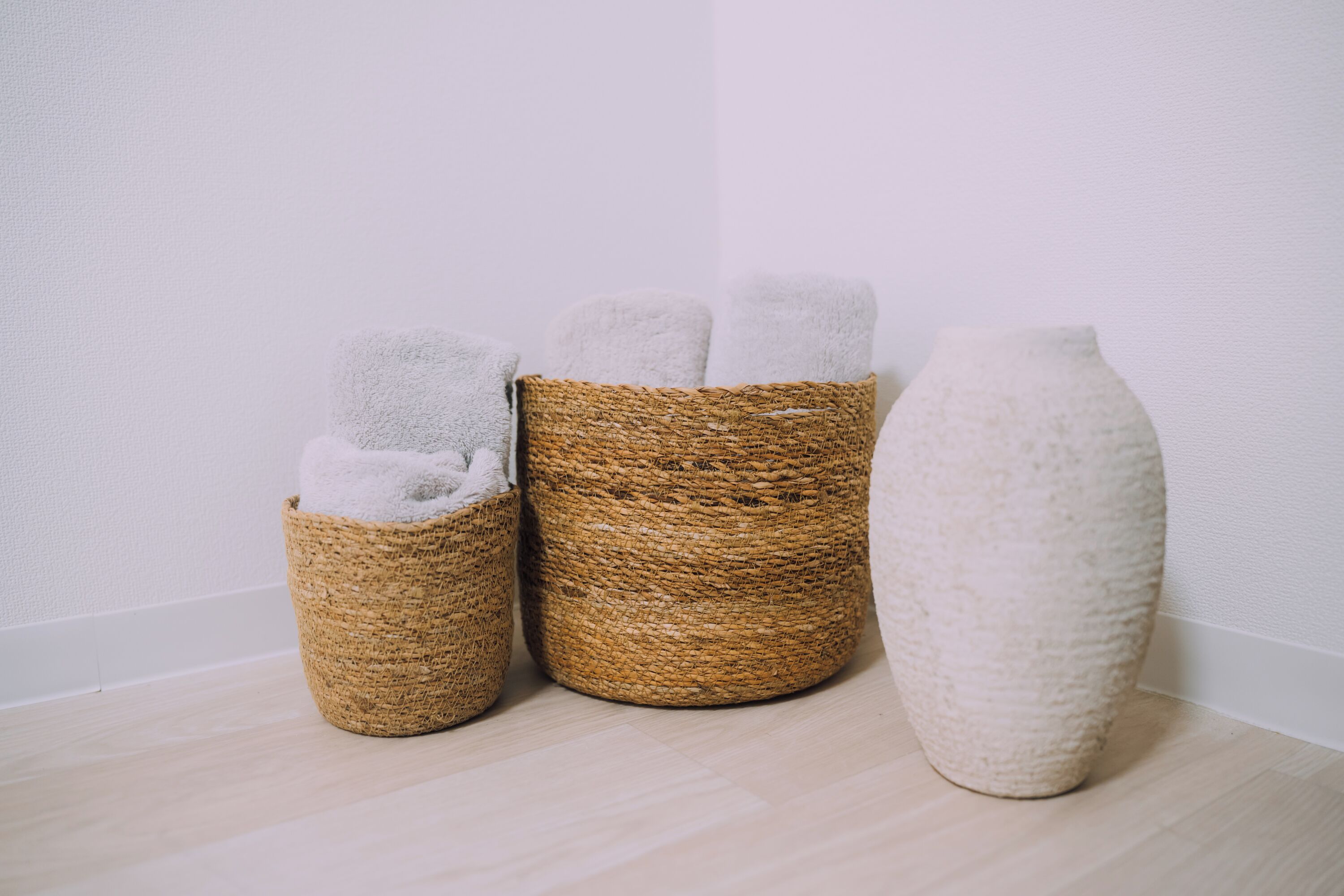 Three woven baskets with towels, one large white vase, and a plain white wall.
