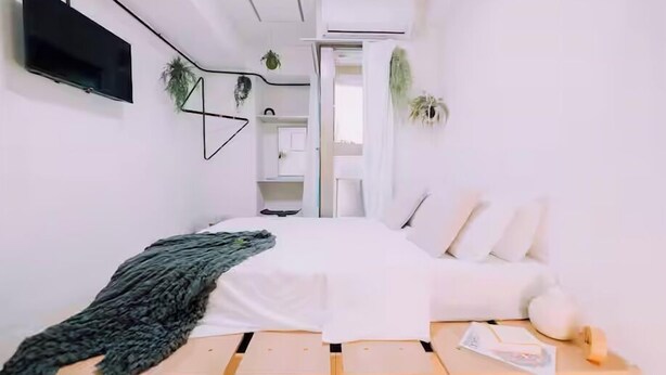 A modern bedroom with a bed, a TV, and a small table with a plant. - Minimalist Loft 1002 (Osaka)