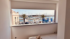 Un dormitorio con un amplio ventanal que da a un puerto deportivo con barcos y un edificio al fondo.