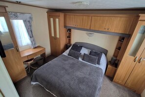 A compact bedroom with a bed, a desk, a wardrobe, and a mirror.